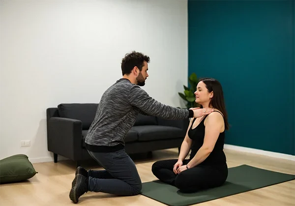 Körpertherapie & Sporttherapie – Achtsamkeitsübung mit Paul Hafemann Paul Hafemann führt somatische Schultermobilisation bei einer entspannten Klientin in einem hellen Behandlungsraum mit dunkel-türkisfarbener Wand und grüner Matte durch.